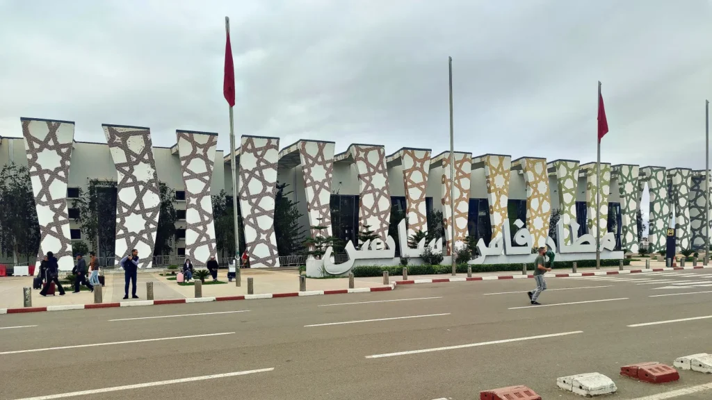 Façade de l'aéroport de Fès-Saïss en journée avec ses piliers inclinés à motifs géométriques et le nom de l'aéroport en lettres arabes
