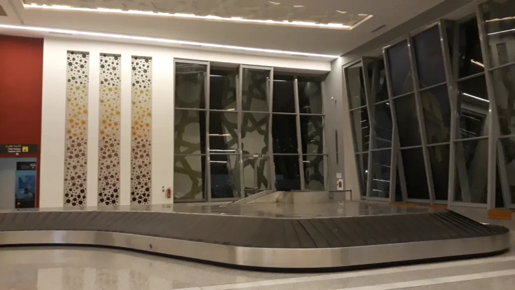 Salle de livraison des bagages de l'aéroport de Fès-Saïss avec un tapis roulant, des panneaux ajourés et des vitrages à motifs géométriques