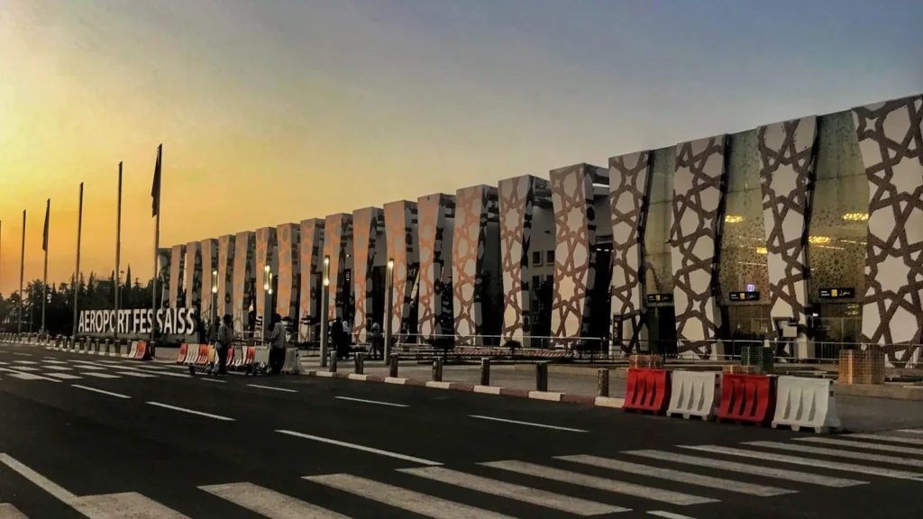 Façade du terminal de l'aéroport de Fès-Saïss au lever du jour, piliers ornés de motifs géométriques et enseigne AEROPORT FES SAISS
