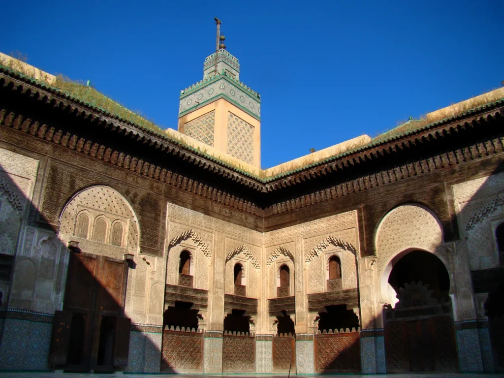 Cour pavée de marbre de la médersa Bou Inania à Fès avec façades en zellige, stuc et cèdre et minaret en arrière-plan