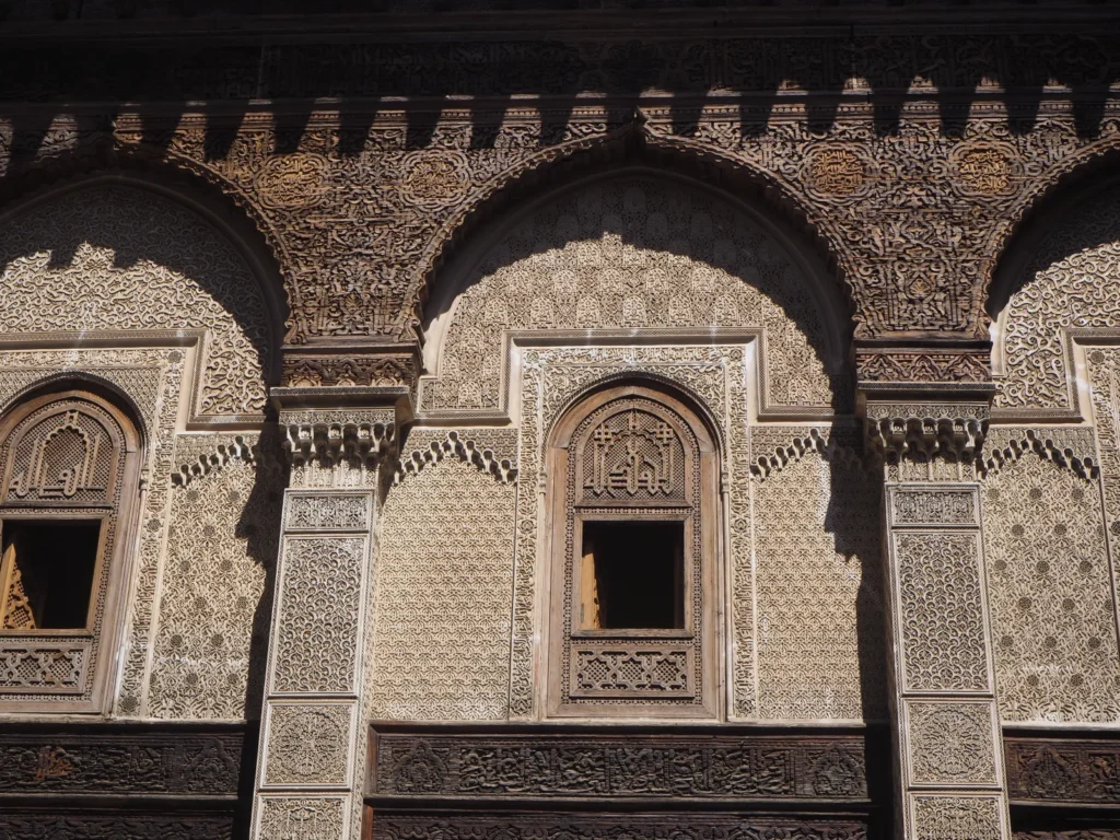 Dettaglio dello stucco scolpito e del cedro cesellato sopra gli archi del cortile della madrasa Al Attarine, con le finestre delle camere degli studenti