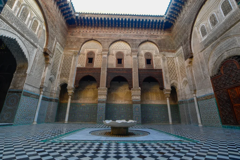 Cortile della madrasa Al Attarine a Fes con vasca di marmo centrale, pavimento a scacchiera e pareti coperte di zellige e stucco scolpito