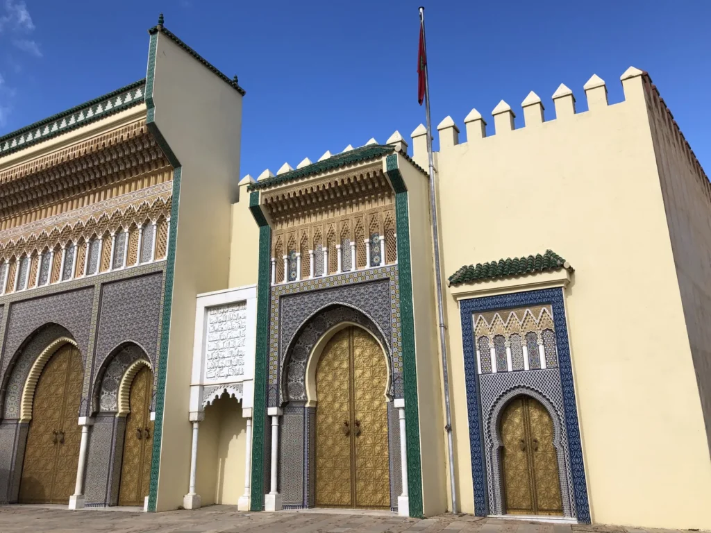 Fachada almenada del Palacio Real de Fez con pabellón lateral, puertas doradas y marco de zellige azul