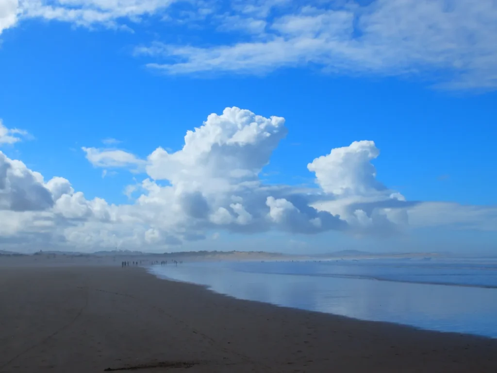 Larga playa de arena húmeda en Essaouira bajo un cielo azul con grandes cúmulos y paseantes a lo lejos