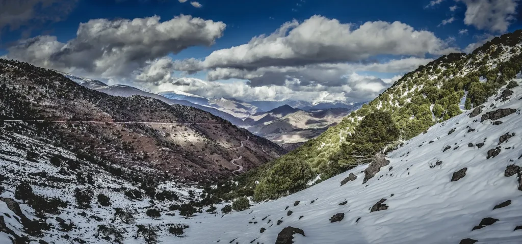 Route de montagne serpentant à flanc de versant dans le Haut Atlas marocain, vallée profonde et sommets en arrière-plan